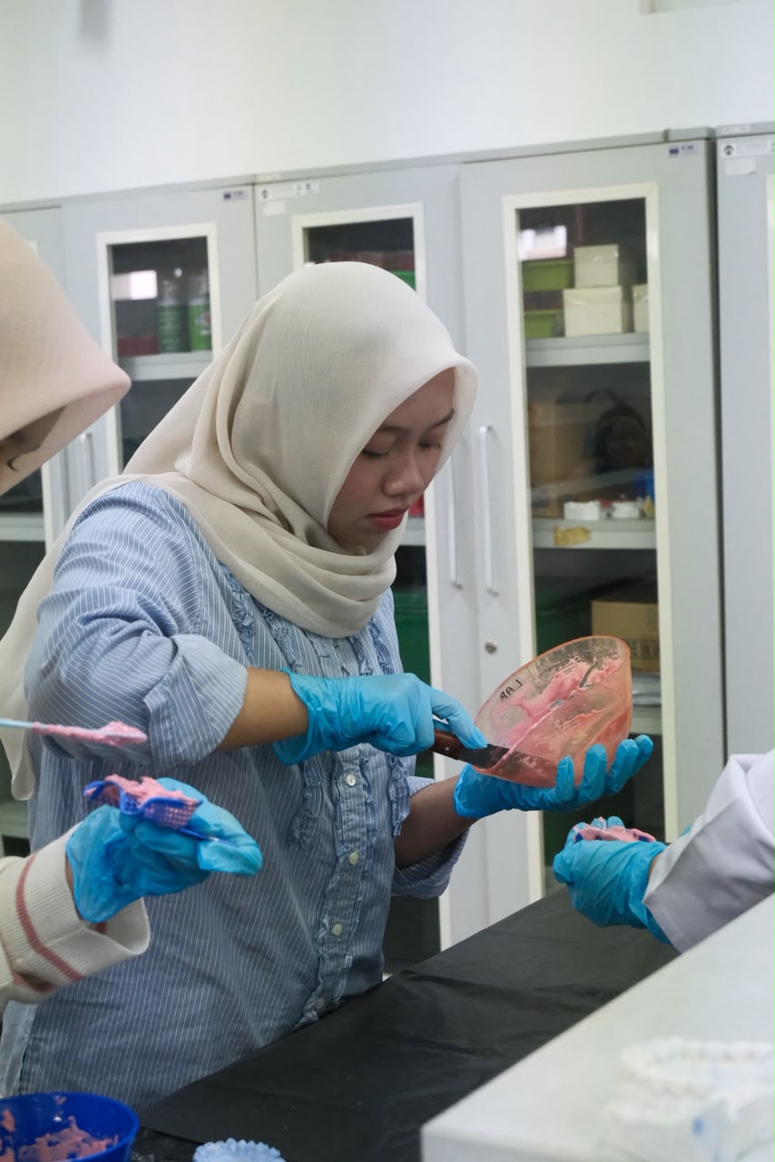 Peserta bersarung tangan mengaduk bahan cetak alginat di sendok cetak saat workshop